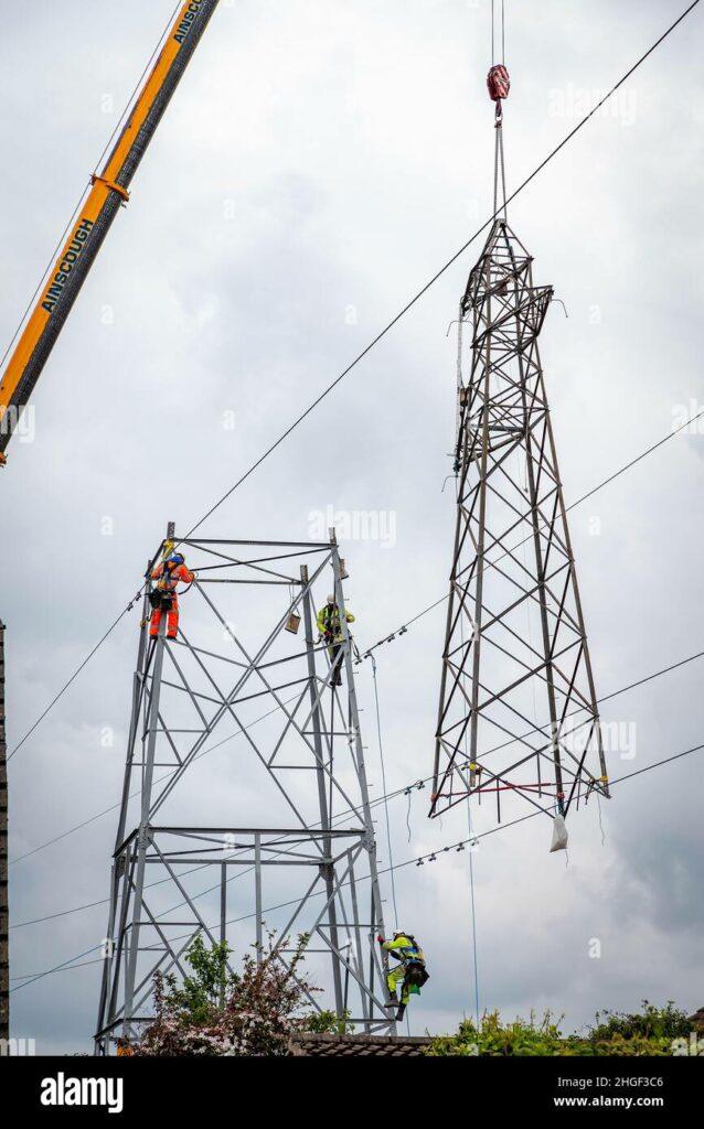 Workmen detach the upper half of an electric pylon which is lowered to the floor by crane for maintenance 2HGF3C6